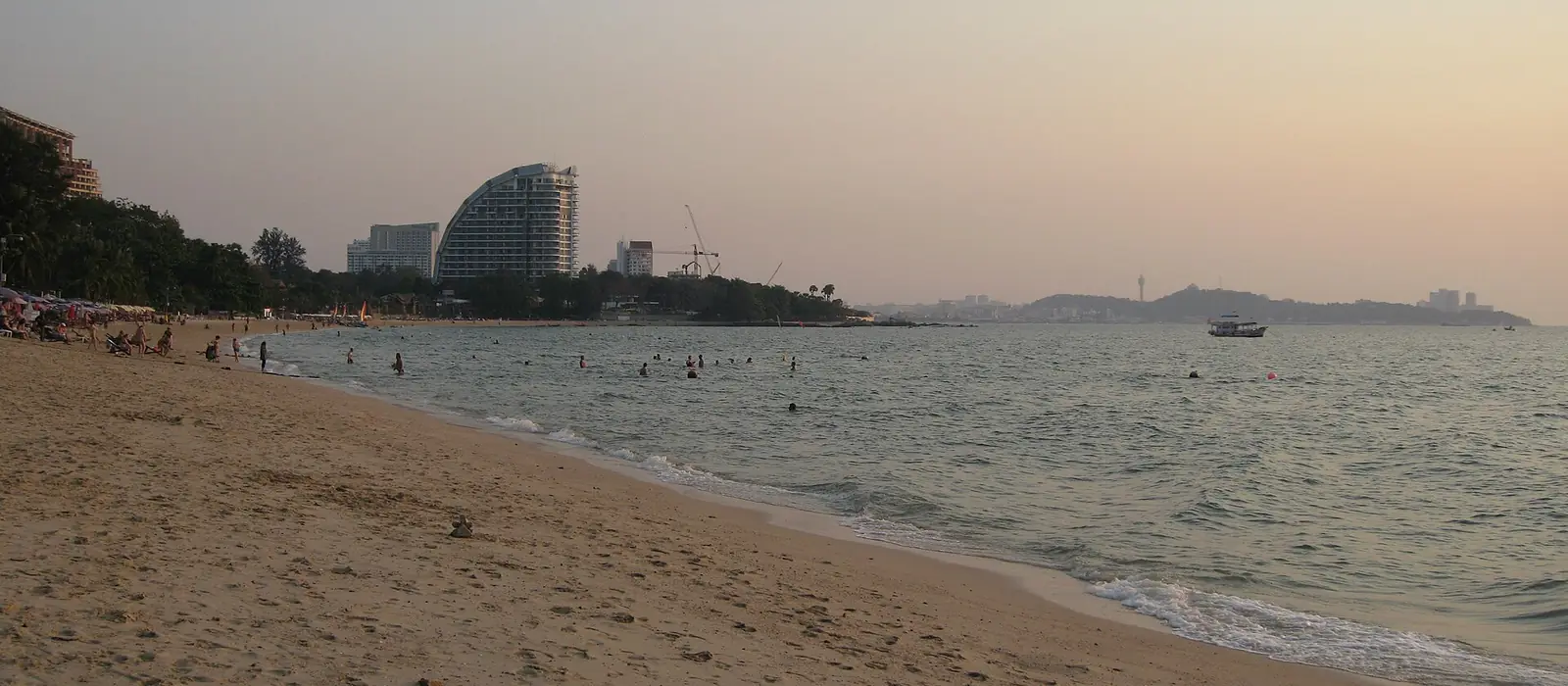 A sandy Naklua beach with calm sea and hotel towers along the shore.